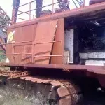 Rusty orange industrial machine with tracks, parked outdoors under a metal structure