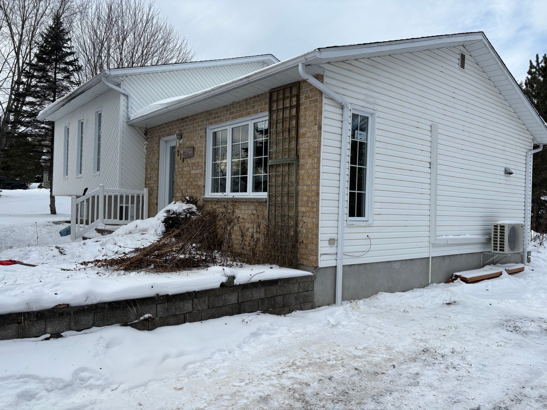 Maison blanche enneigée avec un petit porche et des éléments en pierre en hiver.