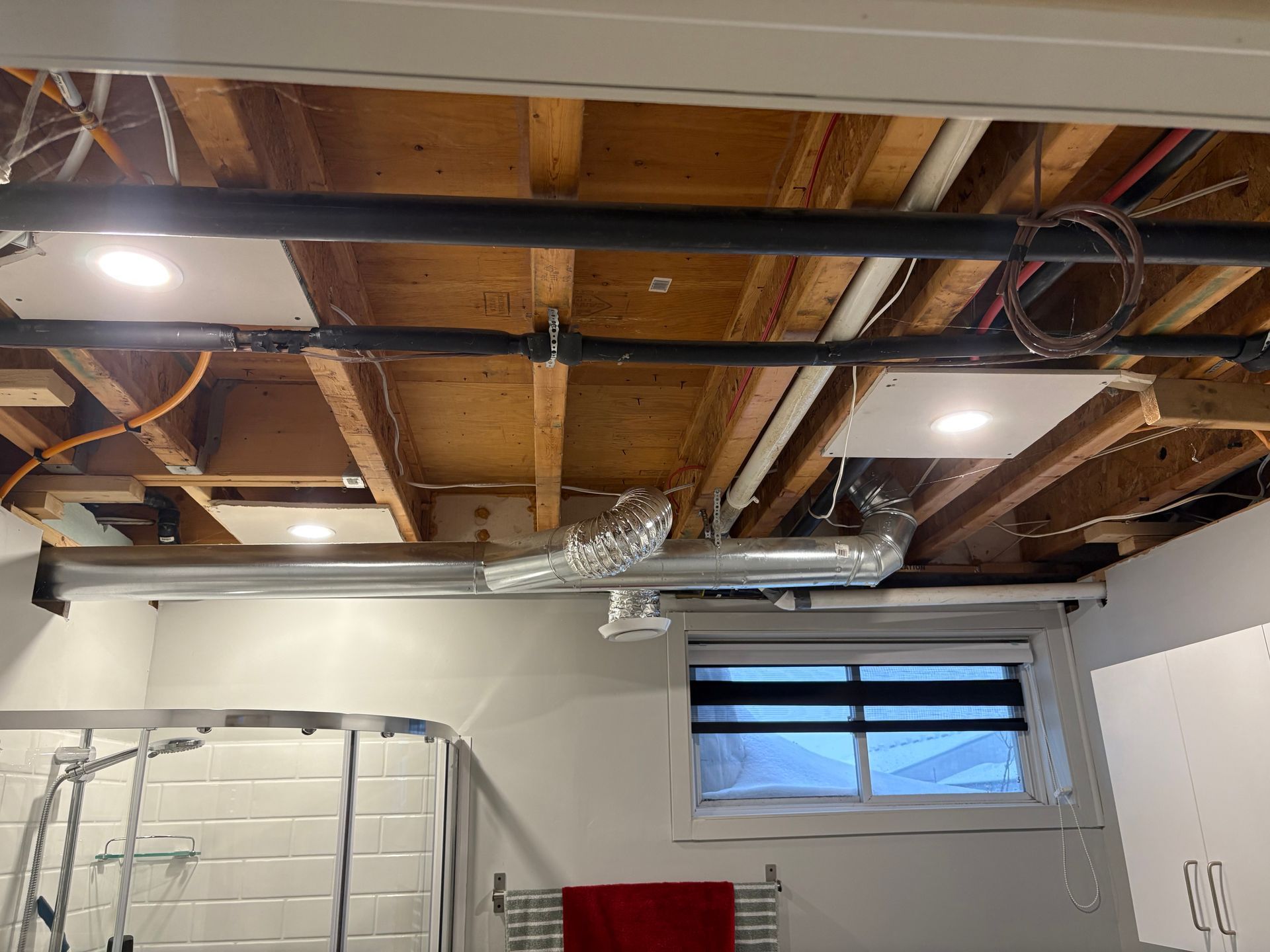 Plafond de sous-sol non aménagé avec poutres en bois apparentes, conduits de ventilation et petite fenêtre près des armoires.