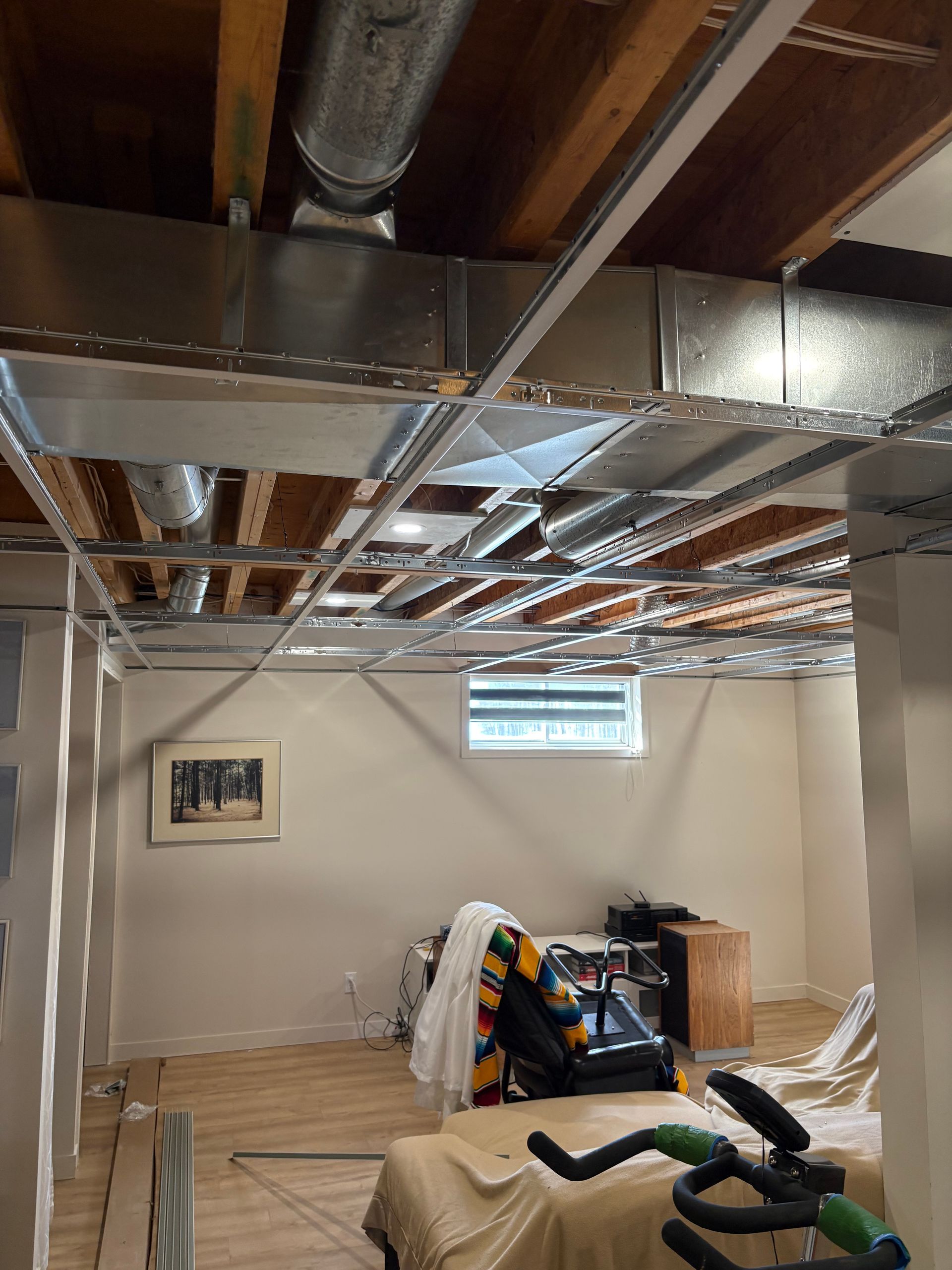 Sous-sol en rénovation avec conduits d'aération apparents, isolation et matériaux de construction éparpillés sur le sol.