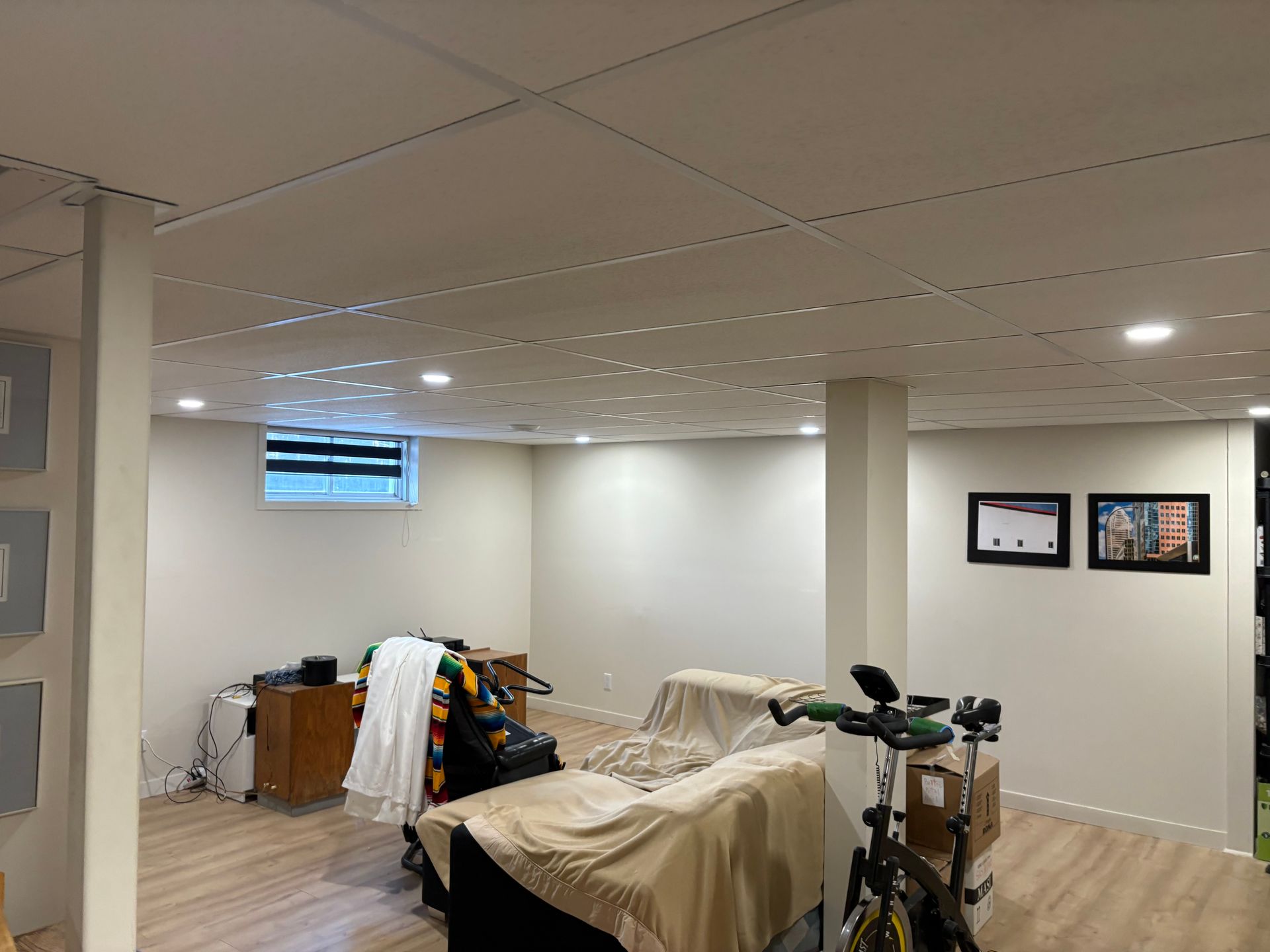 Chambre au sous-sol avec deux lits de camp, une petite fenêtre et des photos encadrées au mur