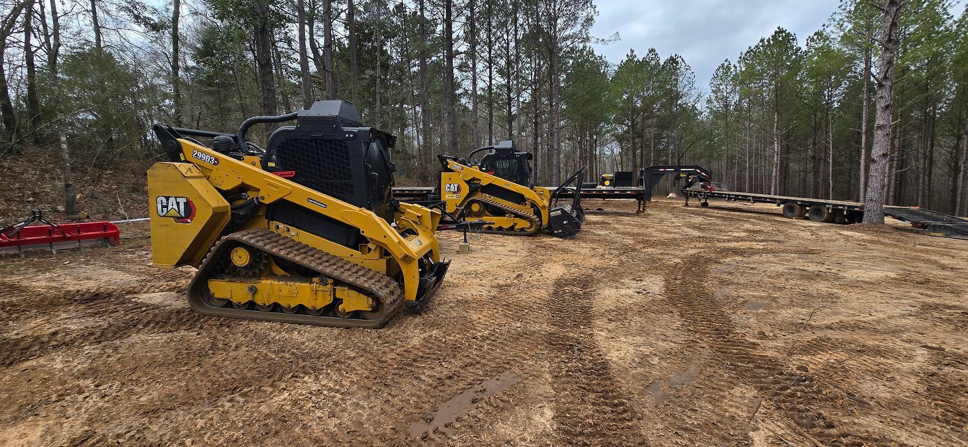 Two yellow Caterpillar skid steer loaders in a wooded clearing.