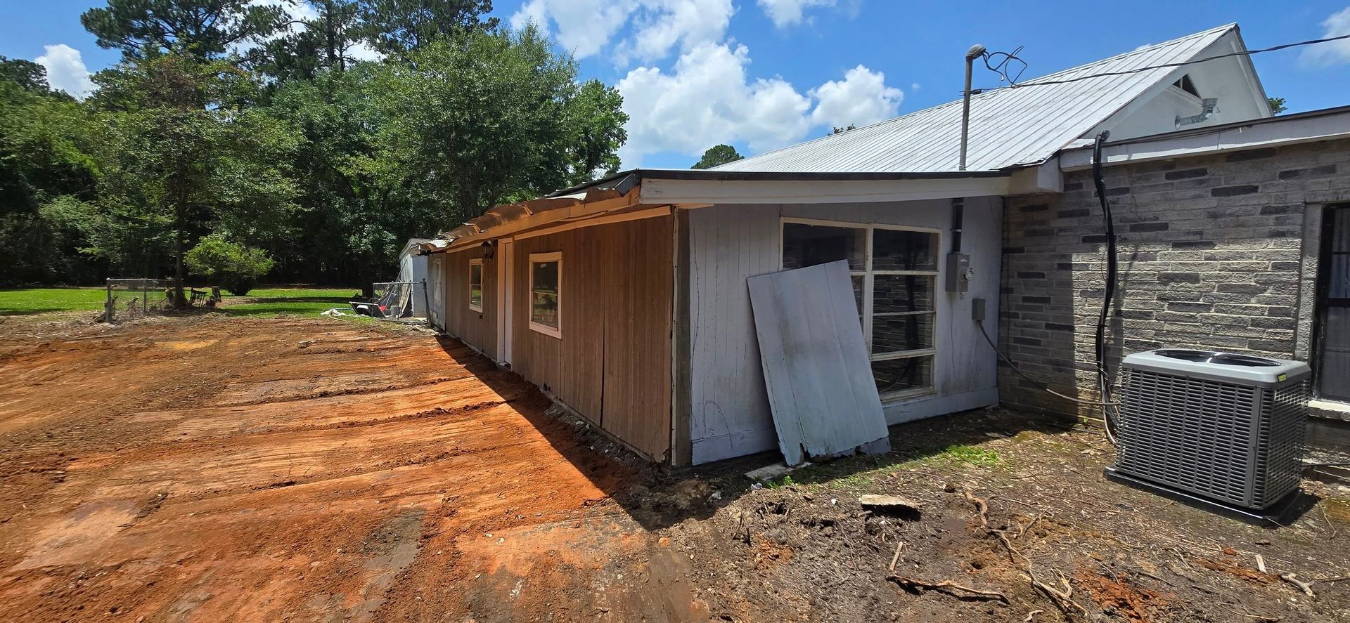 A one-story building with a brown wooden side and a gray stone section. The ground is dirt.