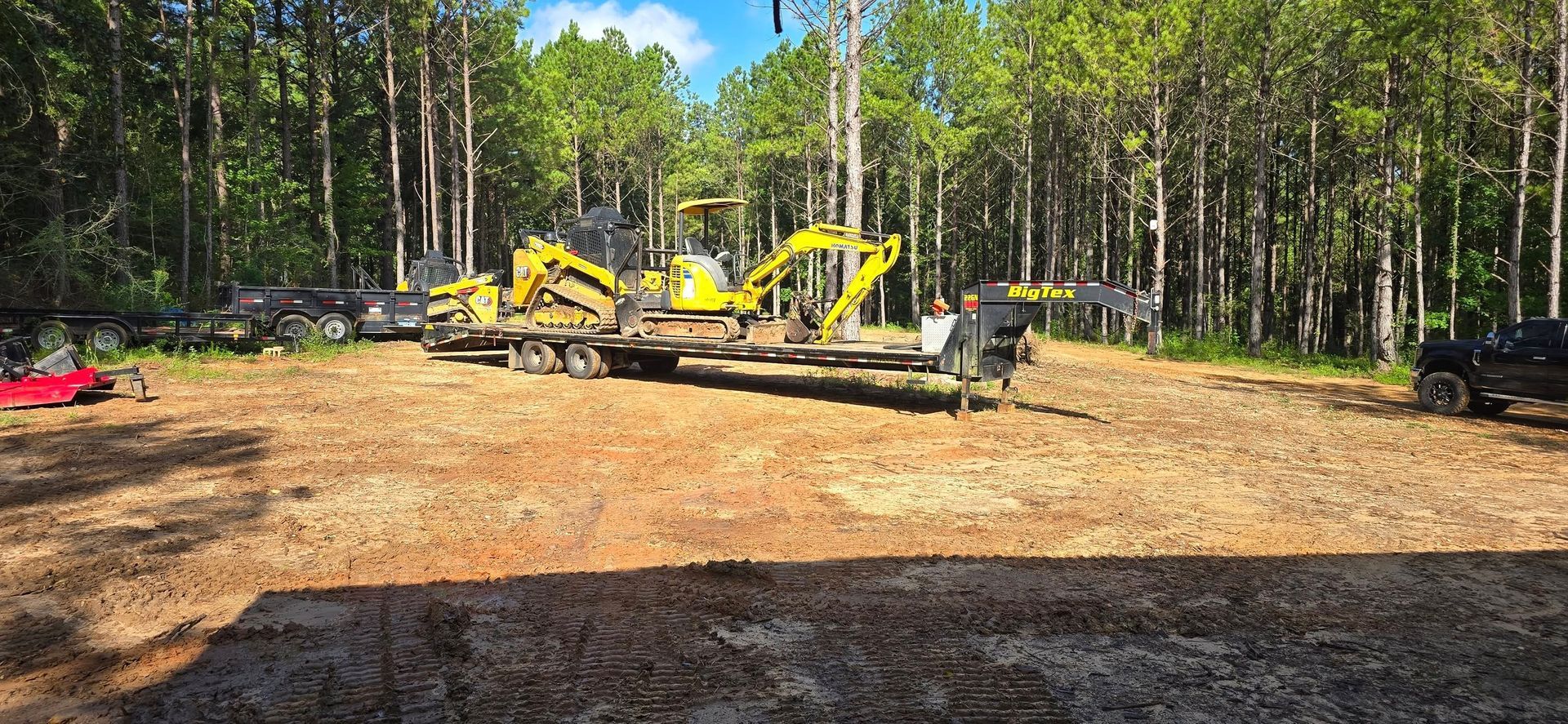Yellow construction vehicles on trailers parked in a clearing near a forest.