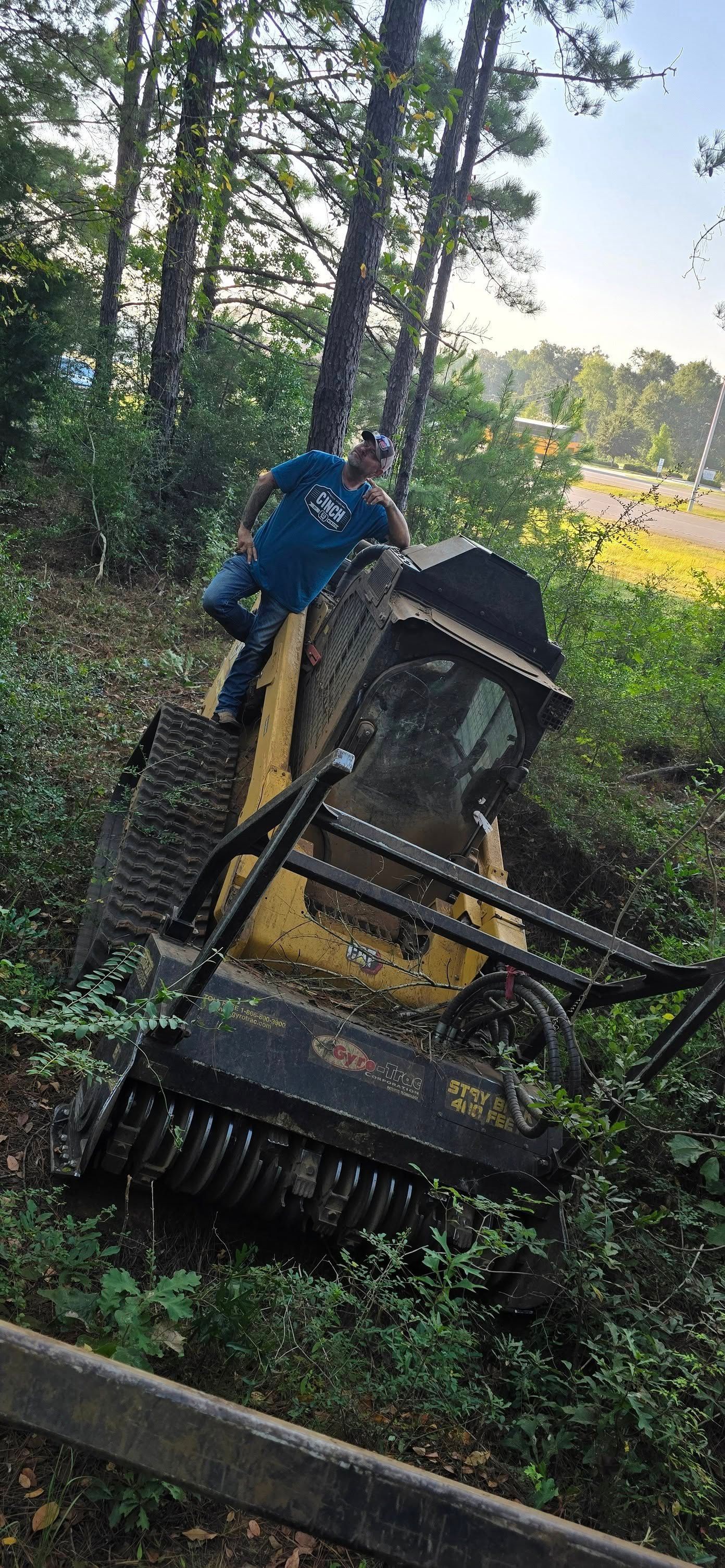 A yellow skid steer tractor is tilted at an angle in the grass, with a person on top.