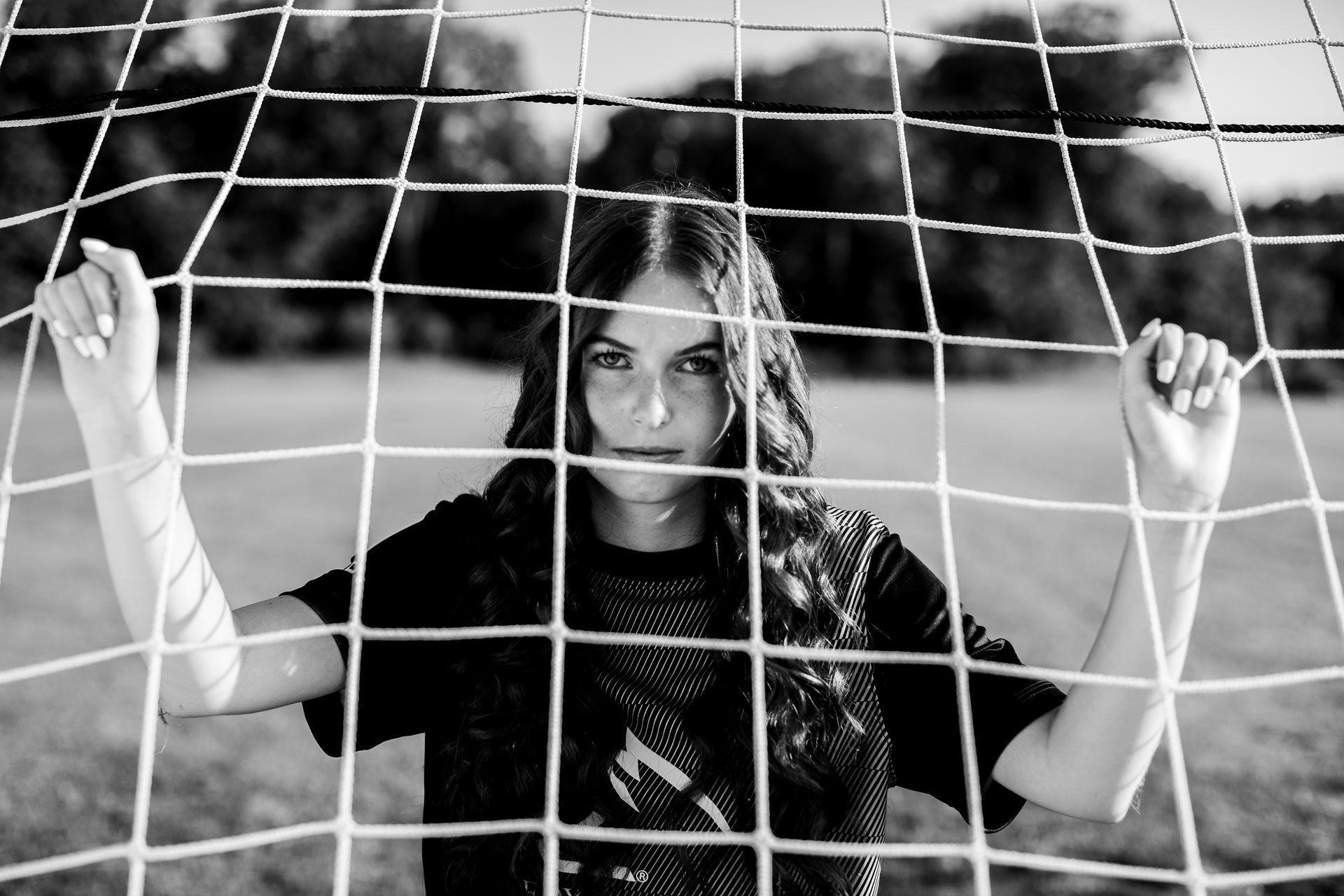 High school senior girl in soccer net on soccer field.