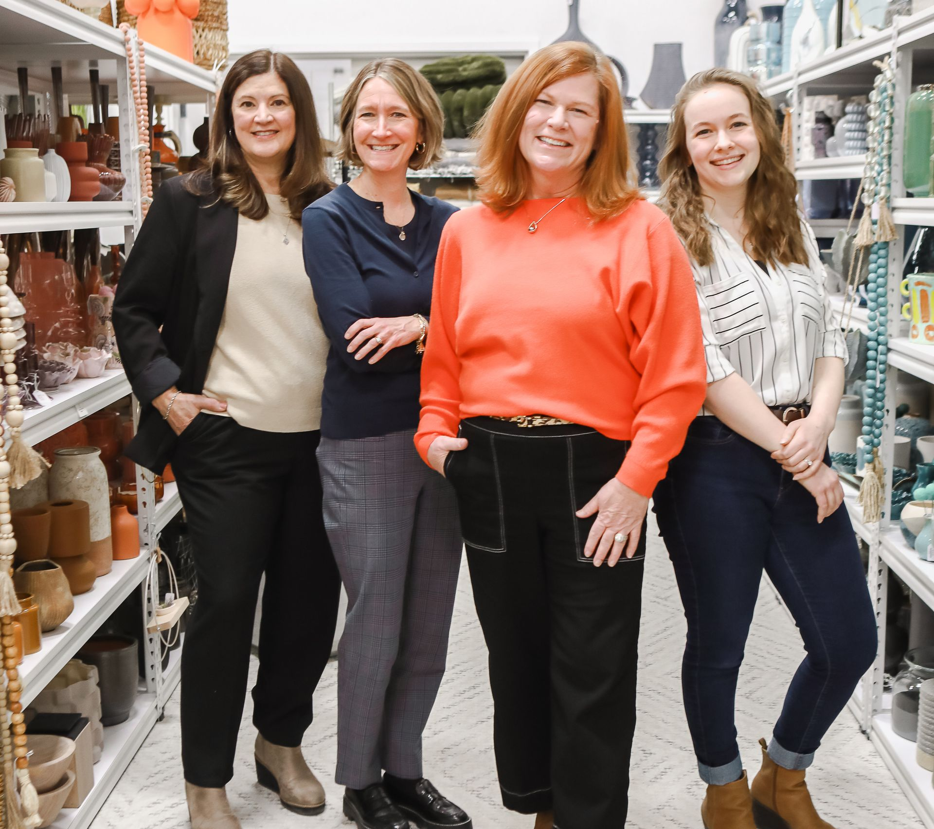 Four people stand smiling together in a store aisle lined with shelves of ceramic home decor items.