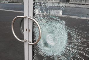 A close up of a broken glass door with a hole in it.