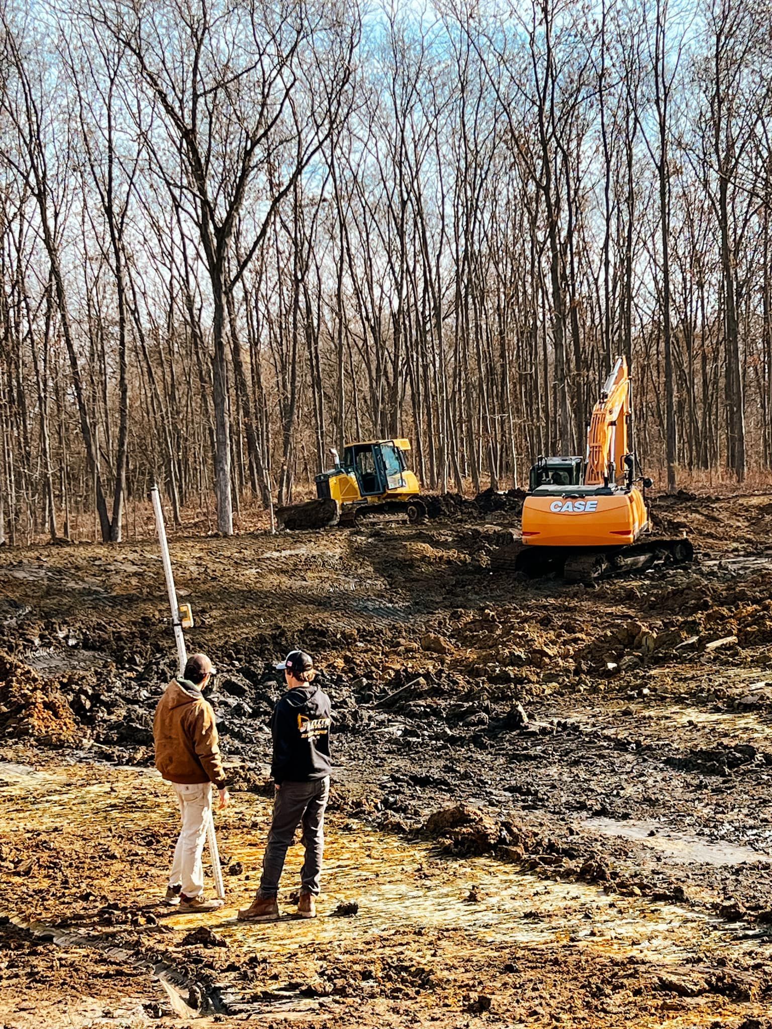 Two men are standing in a field with a bulldozer in the background.