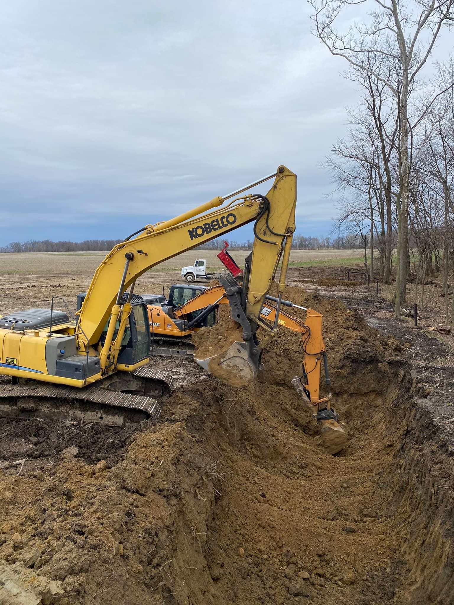 A yellow excavator is digging a hole in the dirt in a field.