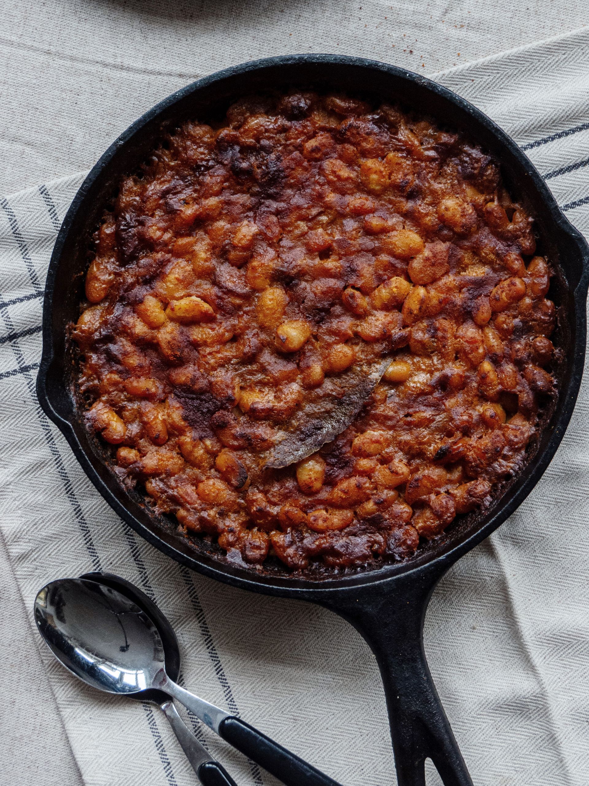 Serbian prebranac, baked beans with onions and paprika, in a black cast iron pan, photo from ZURE-KERSEN-HART