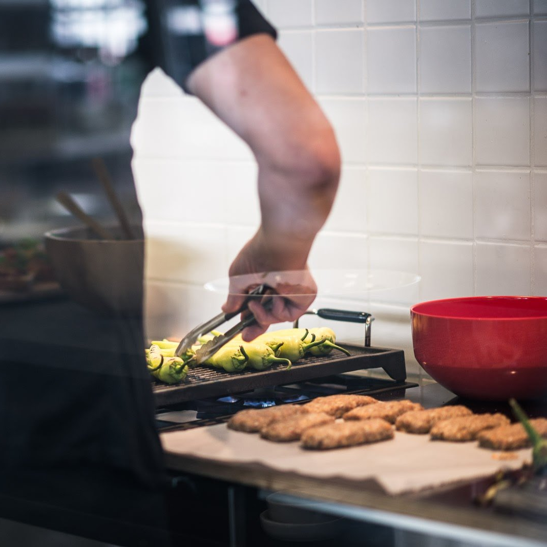 Chef plating grilled vegetables and chicken cutlets in a kitchen with a red bowl nearby