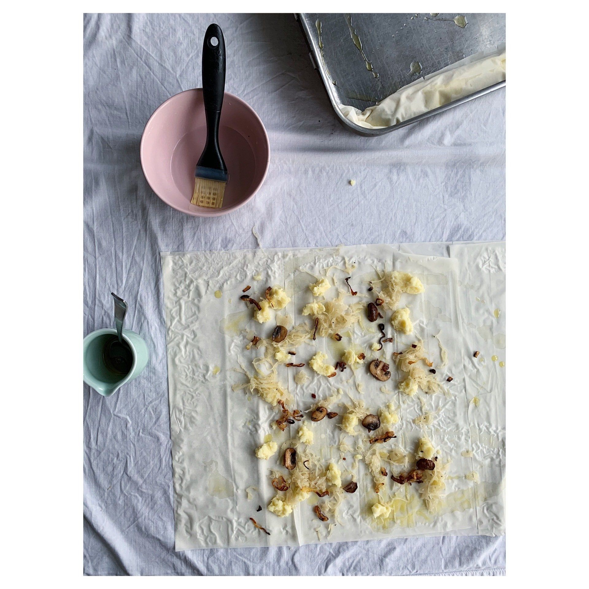 Food on a white cloth with a pink bowl, brush, and a phyllo pastry topped with stamppot, potato, sauerkraut and mushrooms