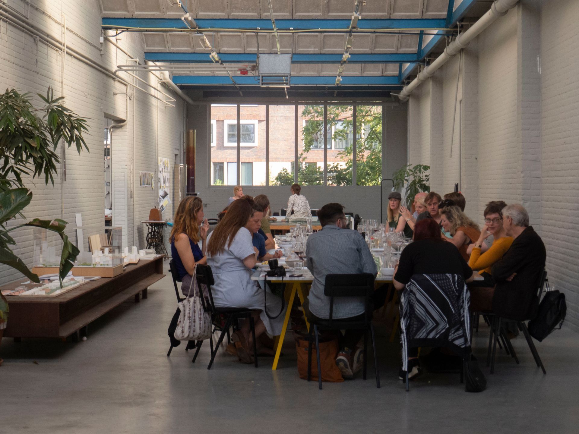 People seated around a long table in a bright industrial-style dining space, don't call me burek