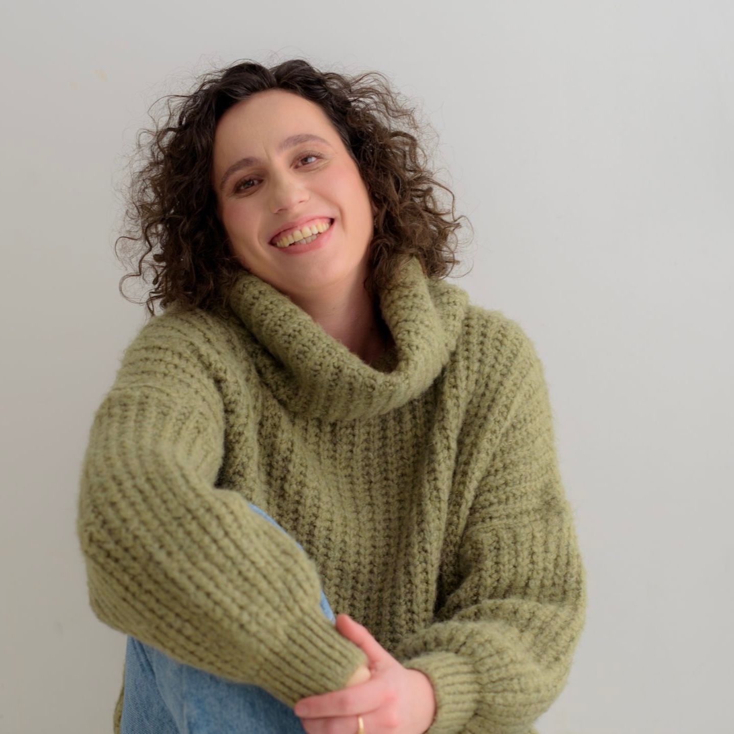 Smiling person in a green knit sweater against a plain light background