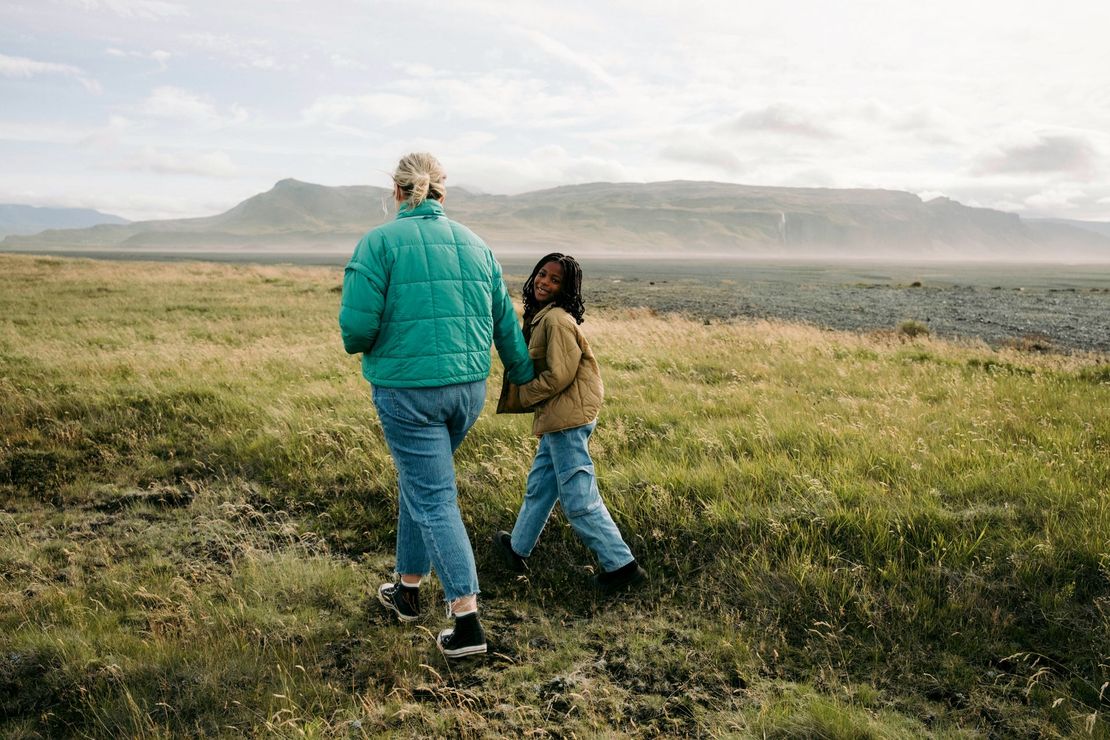 A woman and a child are walking through a grassy field.