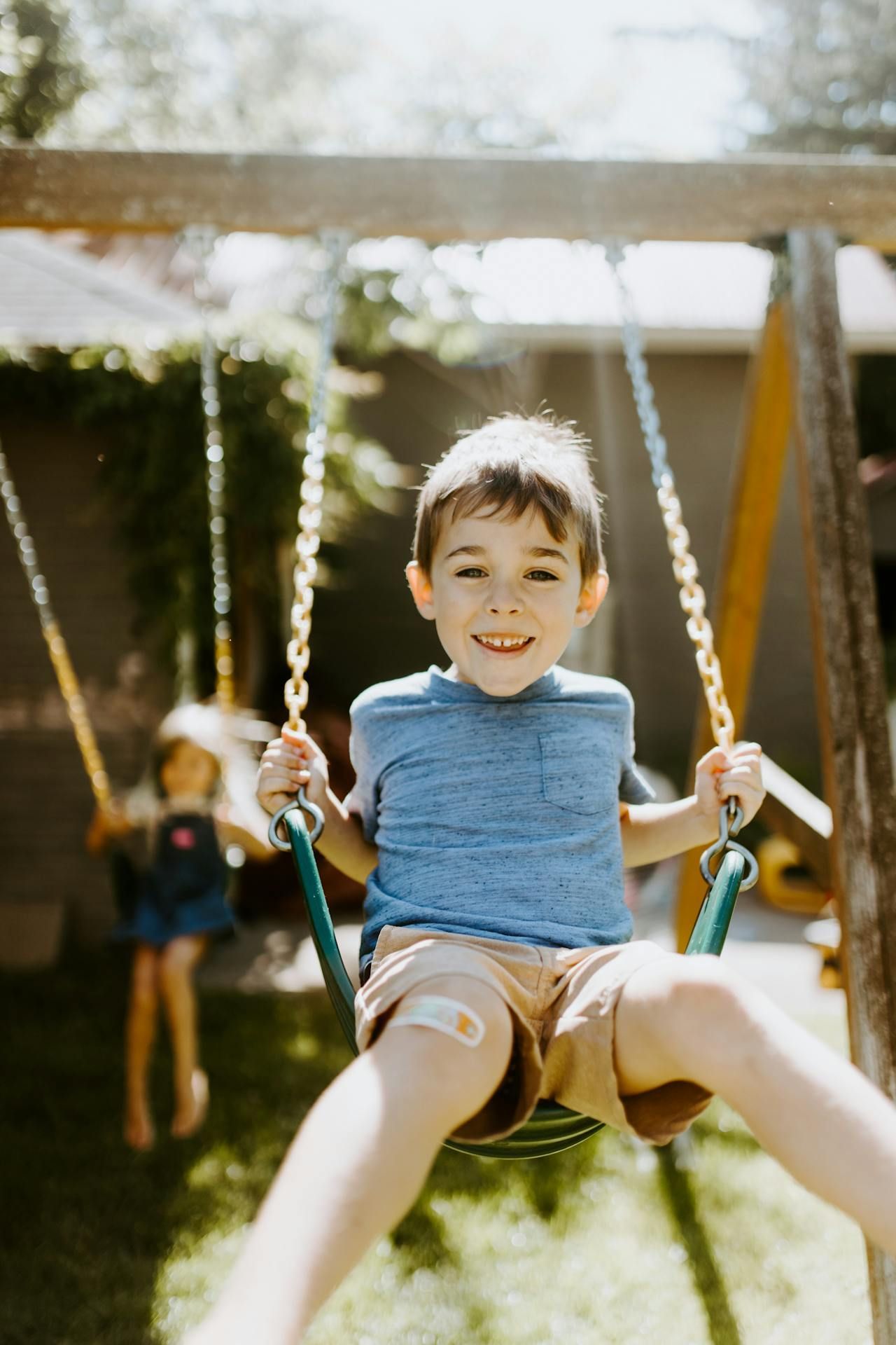 A young boy on a swingset smiling at the camera.