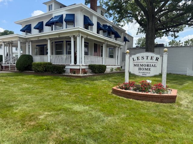 Lester Memorial sign beside a large white house with blue shutters and a manicured lawn