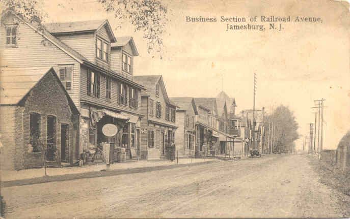 Sepia postcard of a quiet Main Street with storefronts and houses lining a dirt road