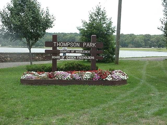 Thompson Park sign in a grassy lakeside park with flowers and trees