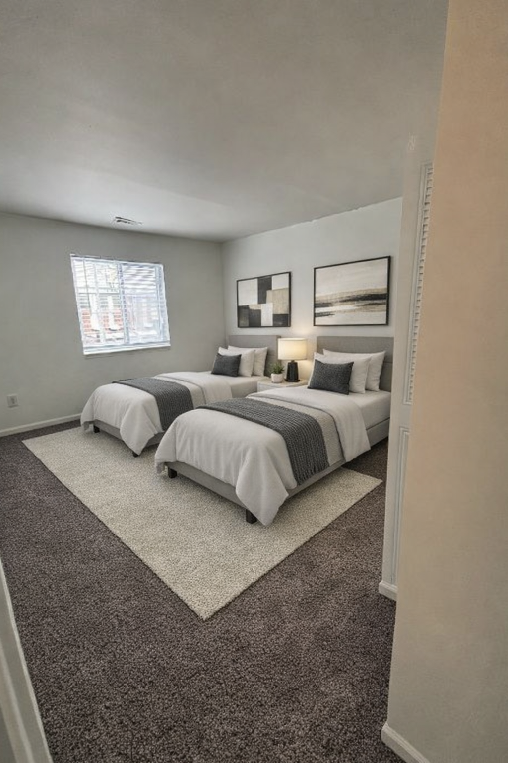 Modern bedroom with two white beds, gray carpet, window, and framed wall art