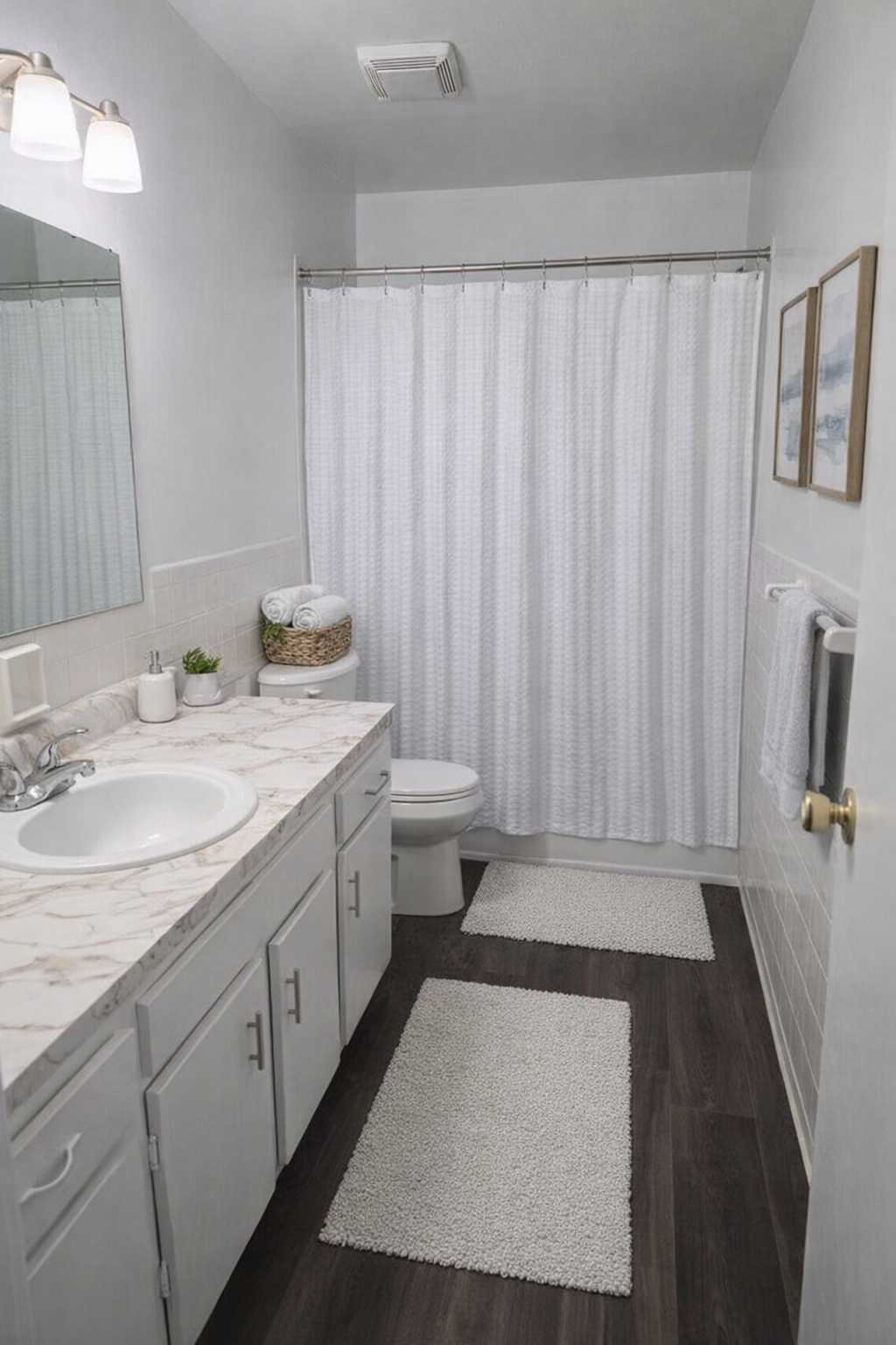 Bright bathroom with white vanity, sink, shower curtain, and striped rugs on dark floor.