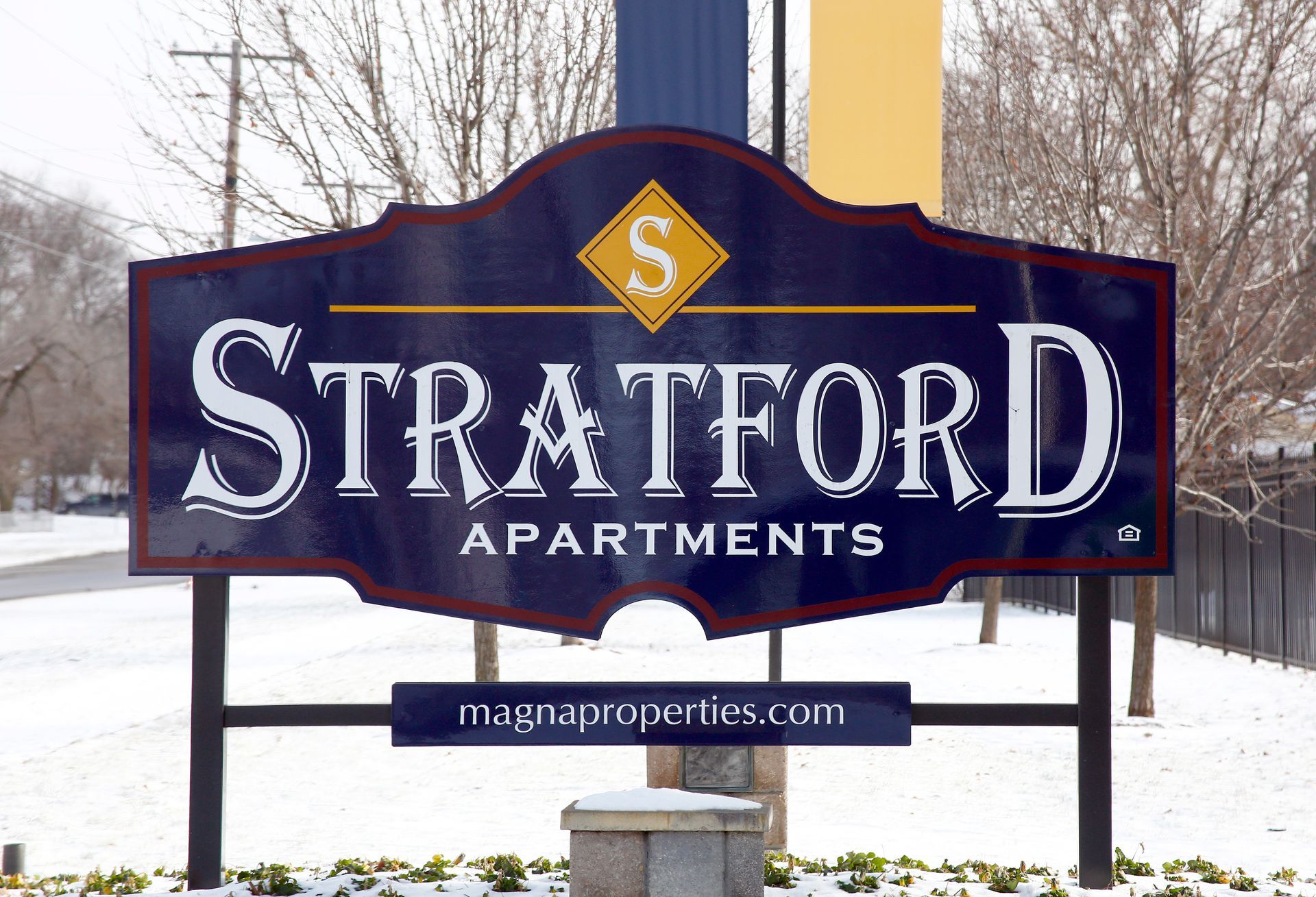 Stratford Apartments sign in white letters on a blue background with a gold emblem, set in a snowy roadside scene