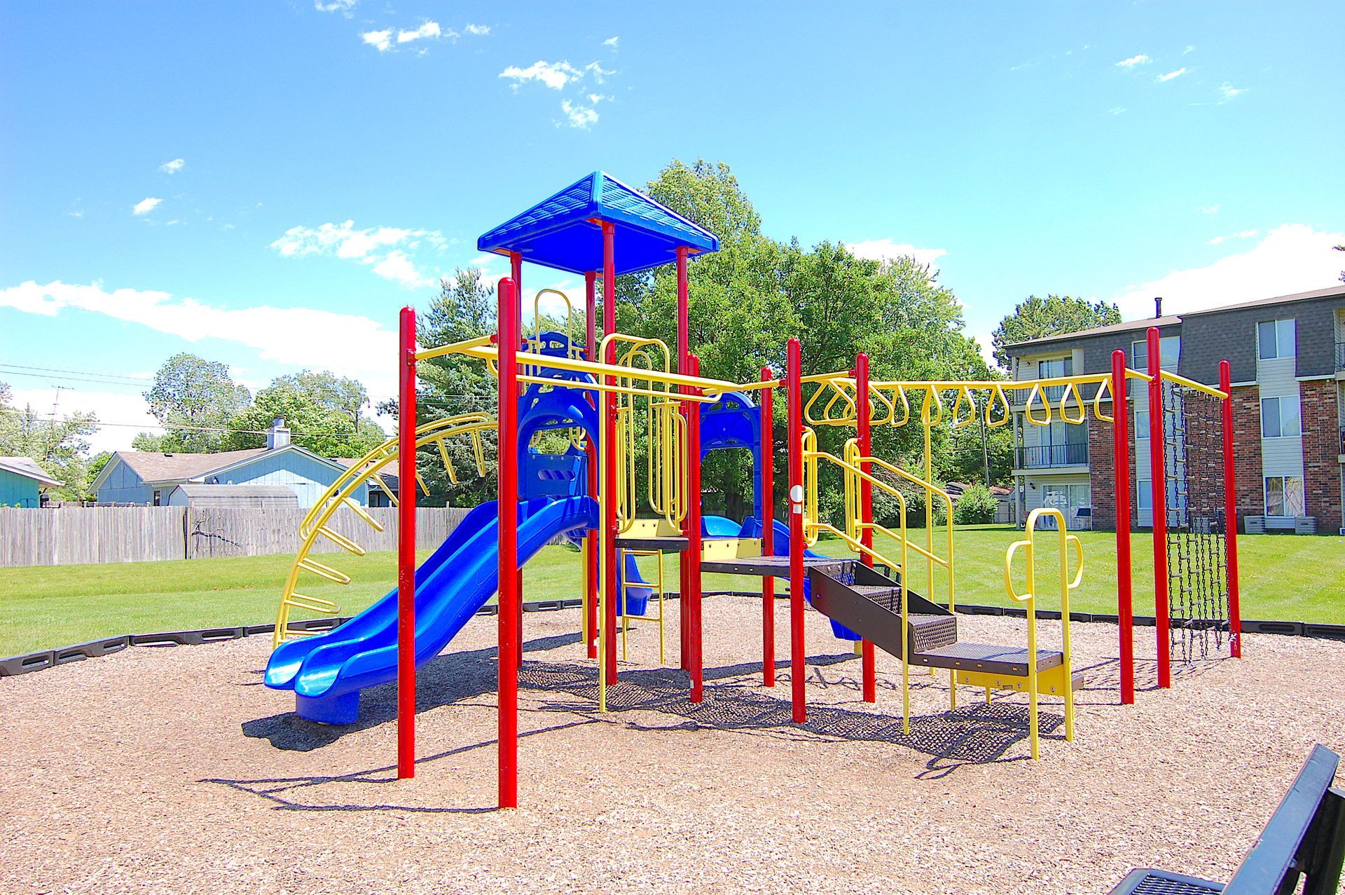 Colorful playground with blue slides, red climbing bars, and a covered platform on a gravel field.