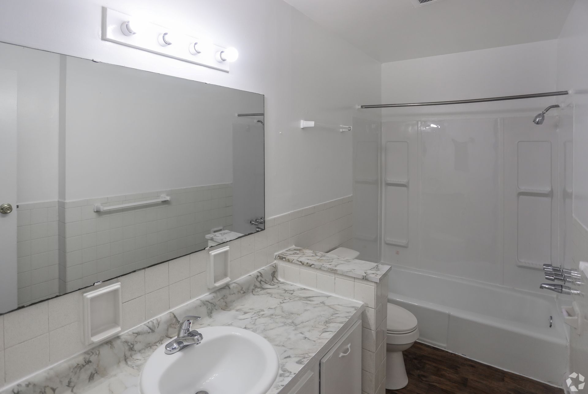 Bright white bathroom with marble vanity, large mirror, sink, and bathtub-shower combo.