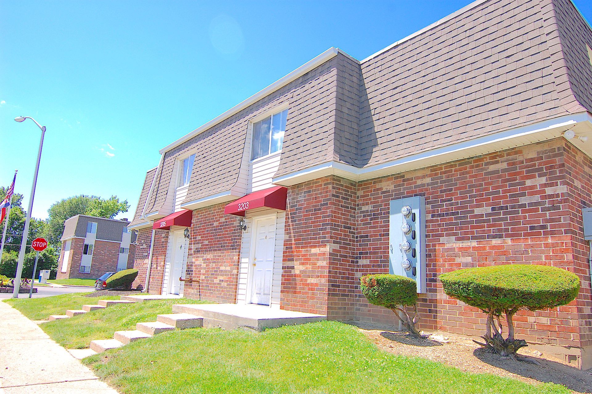 Brick apartment building with red awnings and manicured lawn on a sunny day