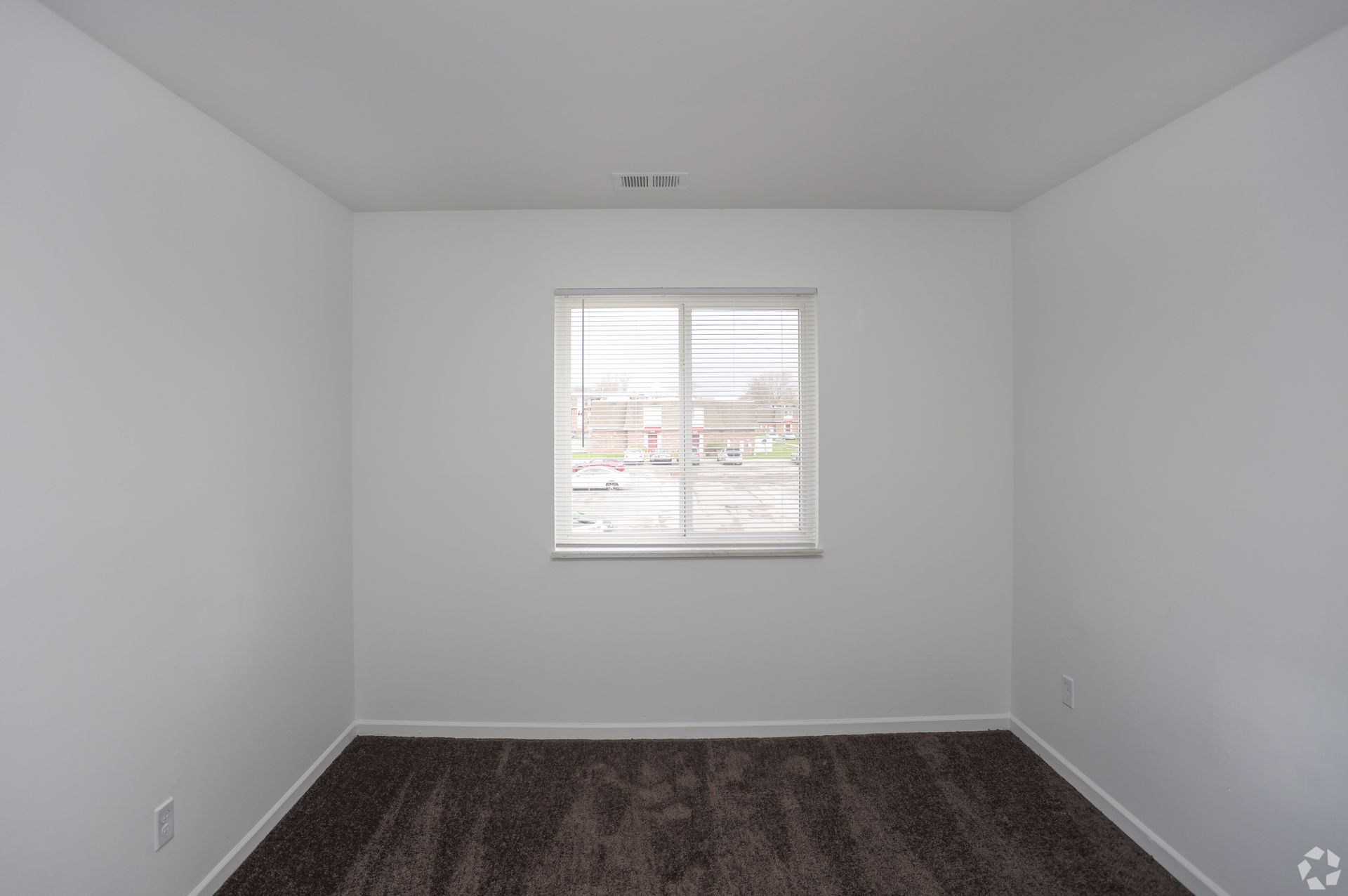 Empty white bedroom with a window and dark carpet flooring