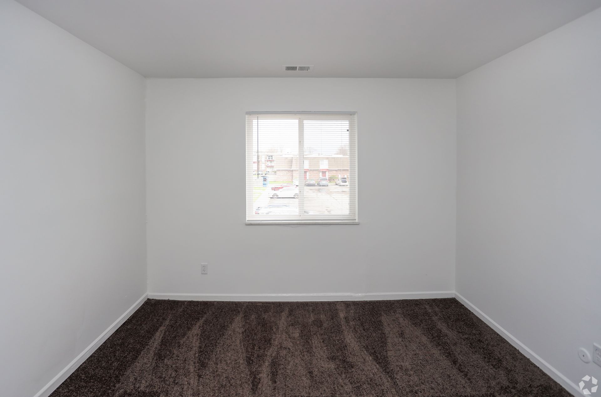 Empty white room with a single window and dark carpet flooring.