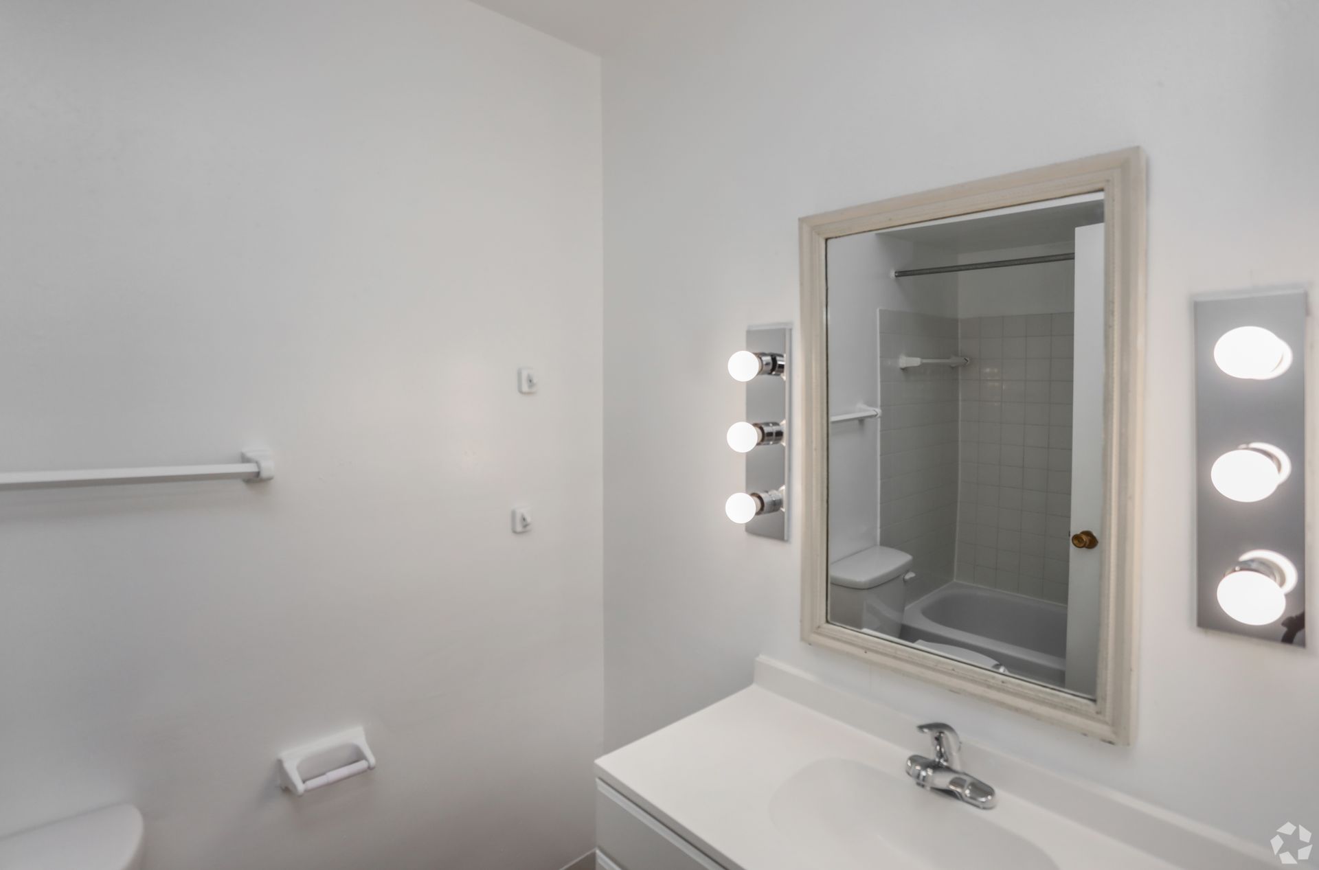 Bright bathroom with white walls, vanity sink, mirror, and vanity lights beside a towel bar.