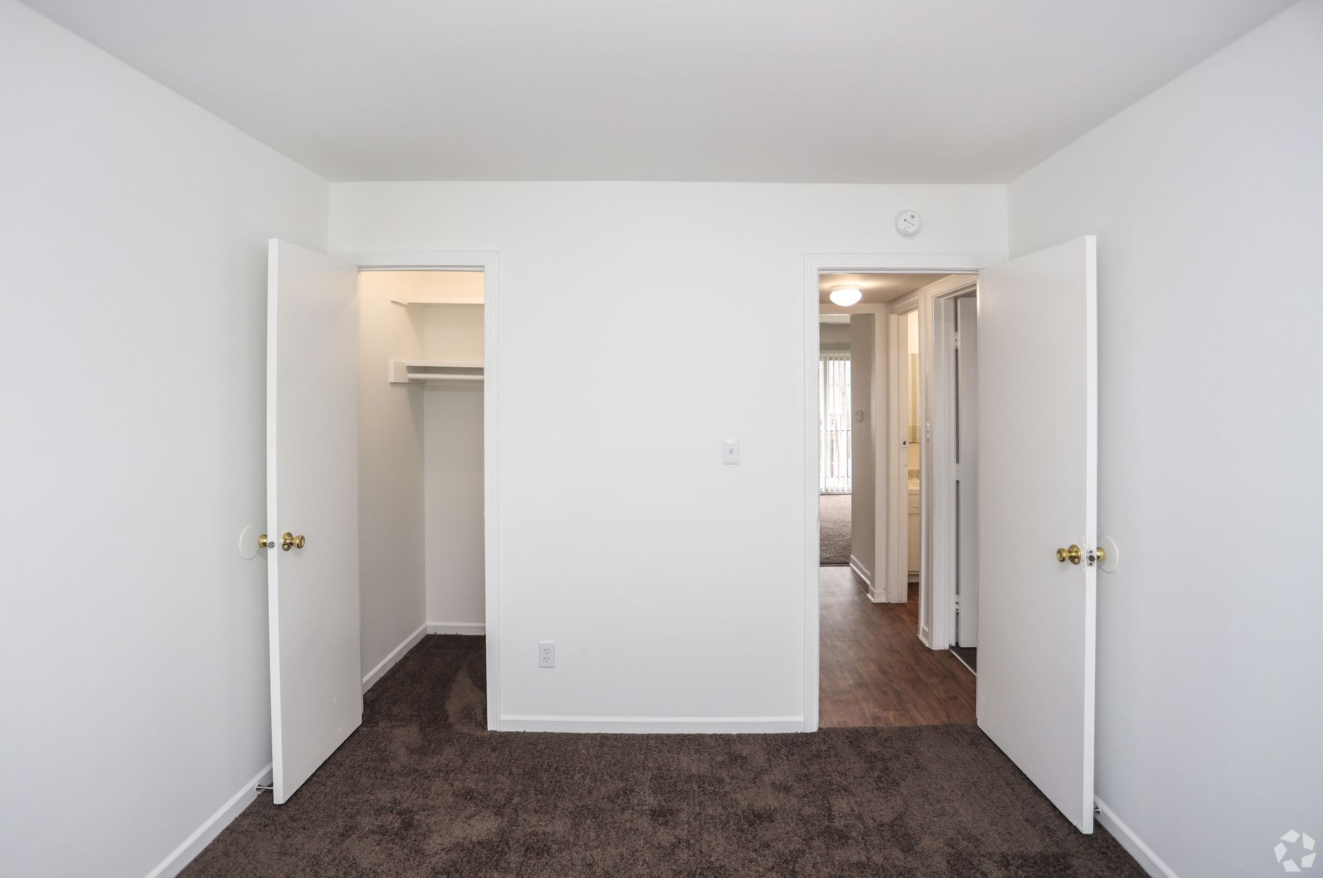 Empty white bedroom with open closet and open double doors leading to a hallway