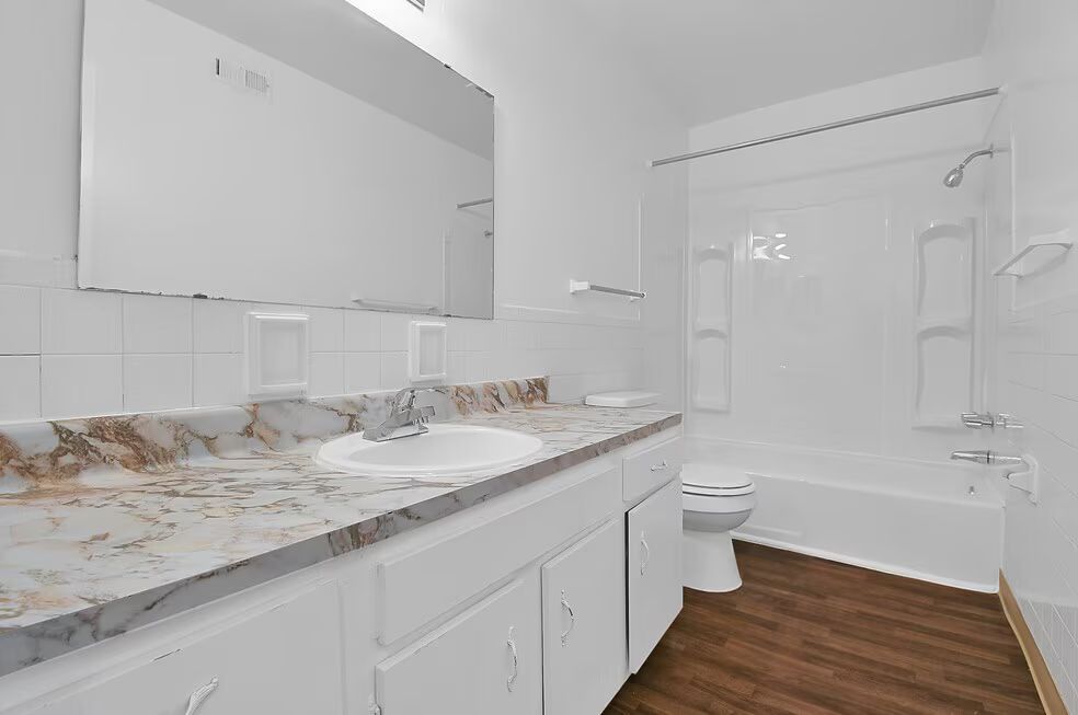Bright bathroom with double vanity, marble countertop, large mirror, and a white tub shower.