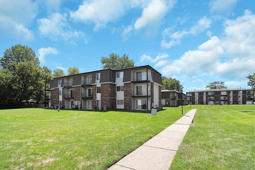 Apartment buildings beside a grassy lawn and sidewalk under a blue sky