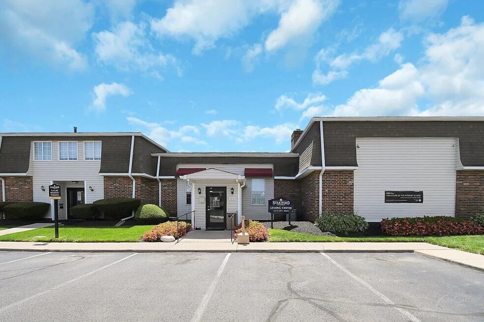 Residential building entrance with a central doorway, white siding, and flower planters under a blue sky