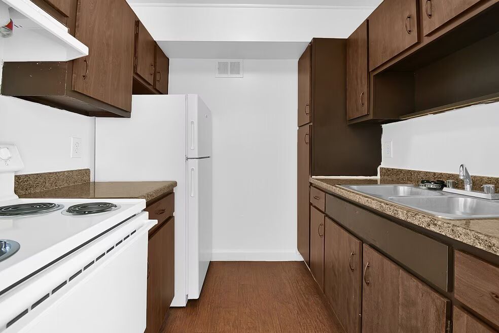 Narrow kitchen with white appliances, brown cabinets, and granite countertops along both sides