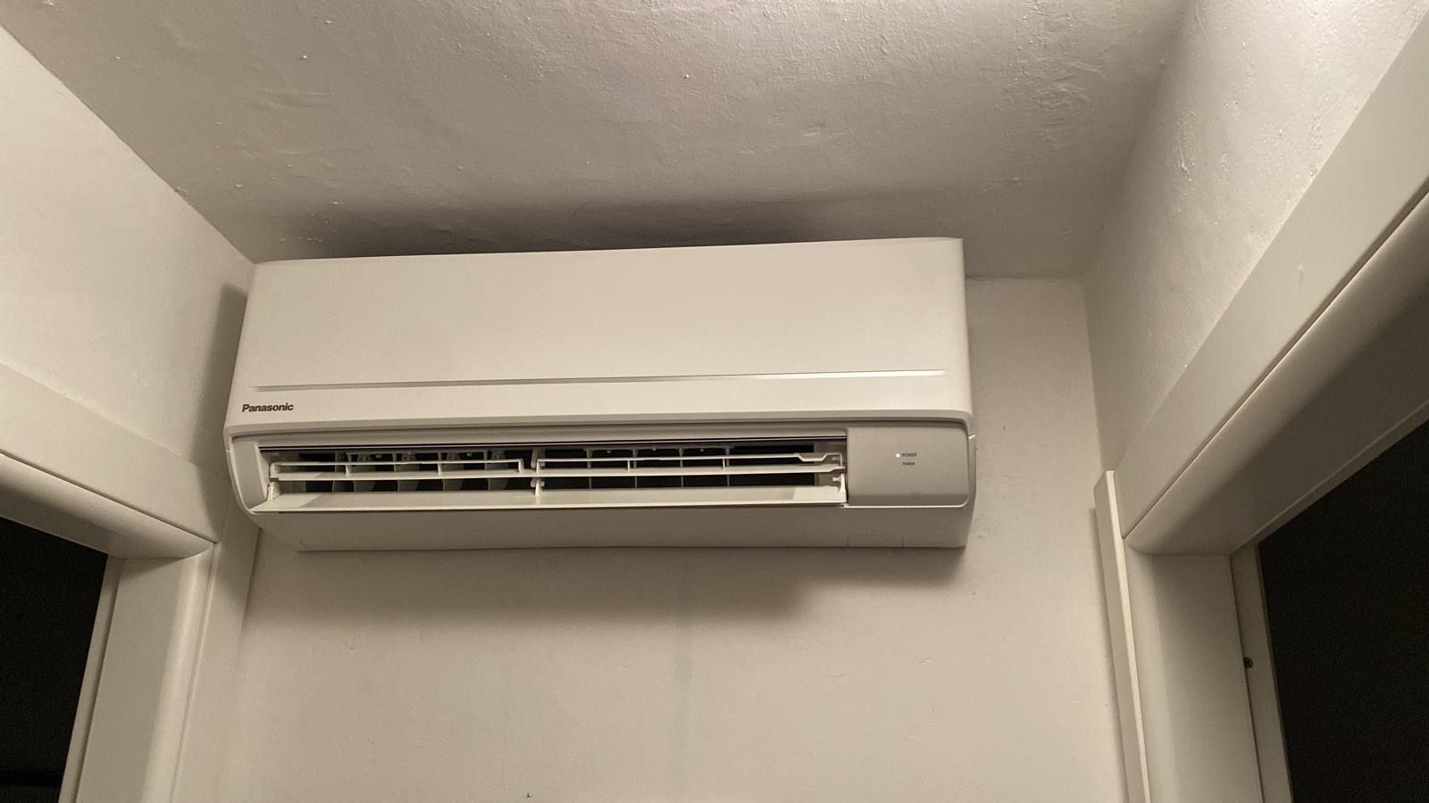 Condizionatore d'aria bianco a parete sopra una porta in un corridoio beige.
