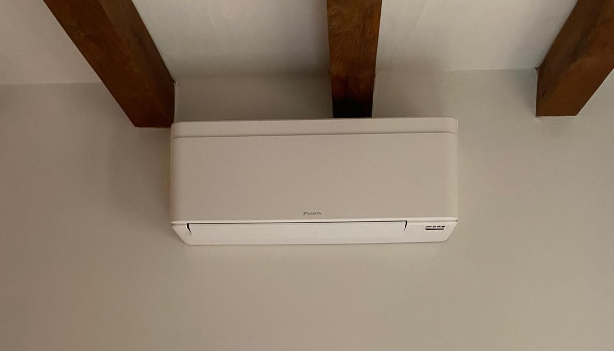 Condizionatore d'aria bianco a parete, installato sotto le travi di legno a vista del soffitto.