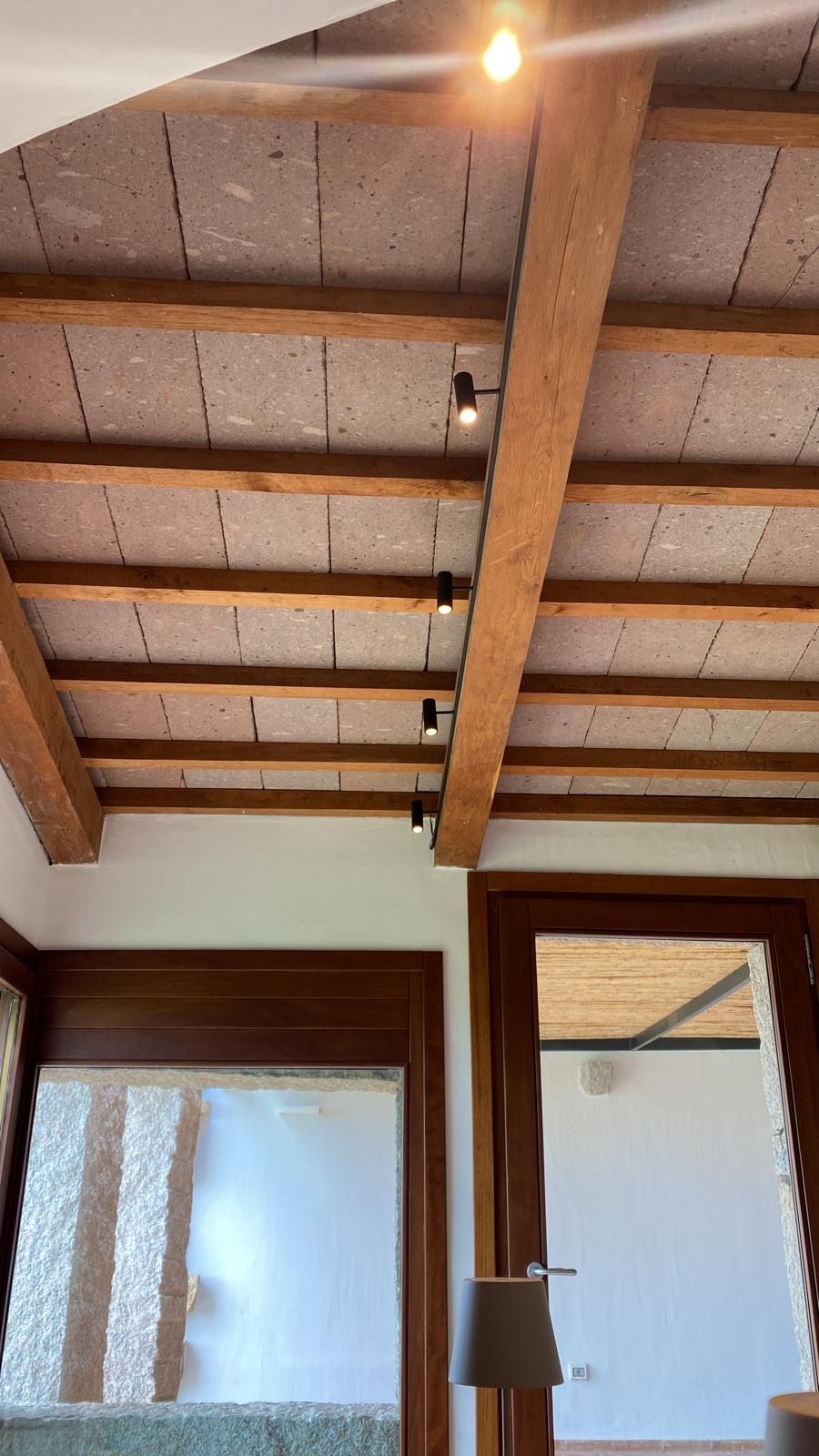 Soffitto con travi in legno a vista e lampade a sospensione sopra una stanza con finestre smerigliate.