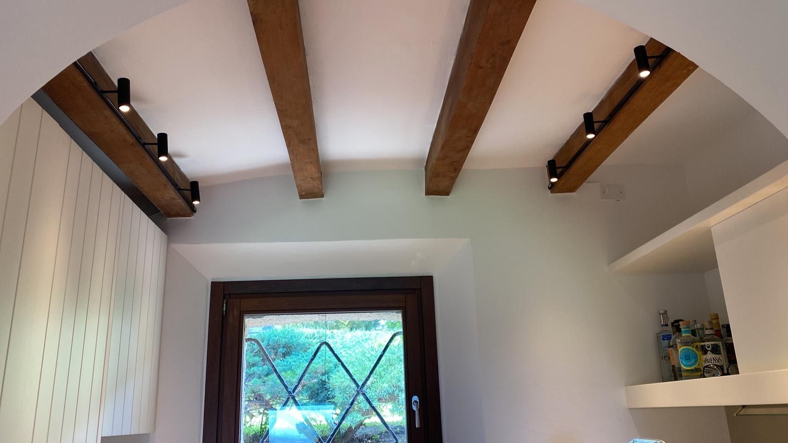 Interno con pareti bianche, travi in legno a vista sul soffitto e una piccola finestra con vetro decorato a rombi.