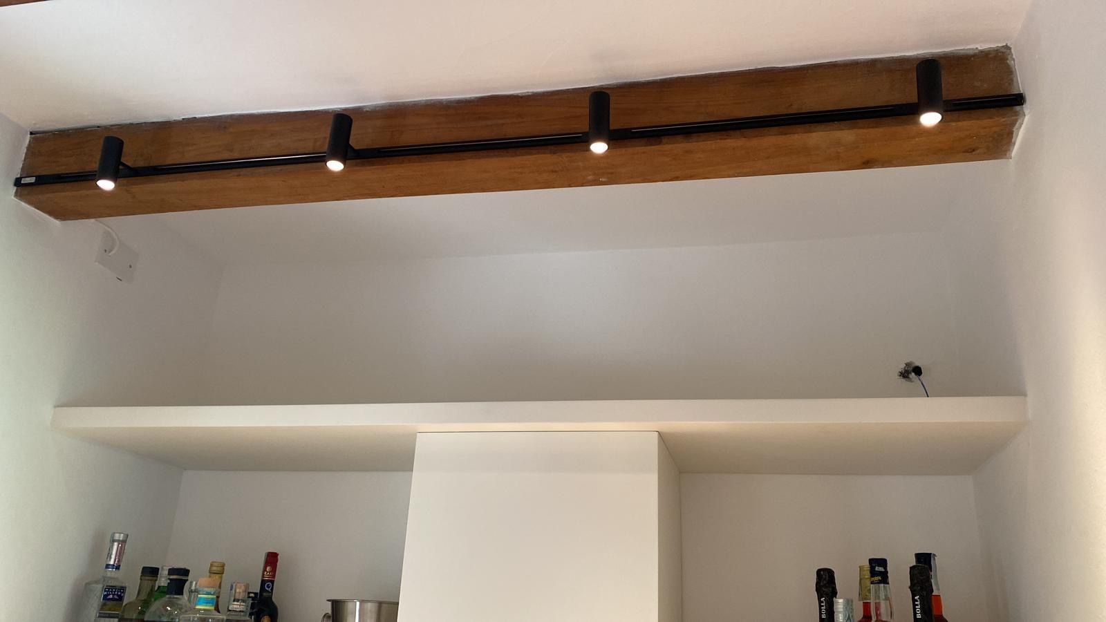 Parete bianca con una lunga mensola e lampadario in legno sopra un bancone o un angolo bar.