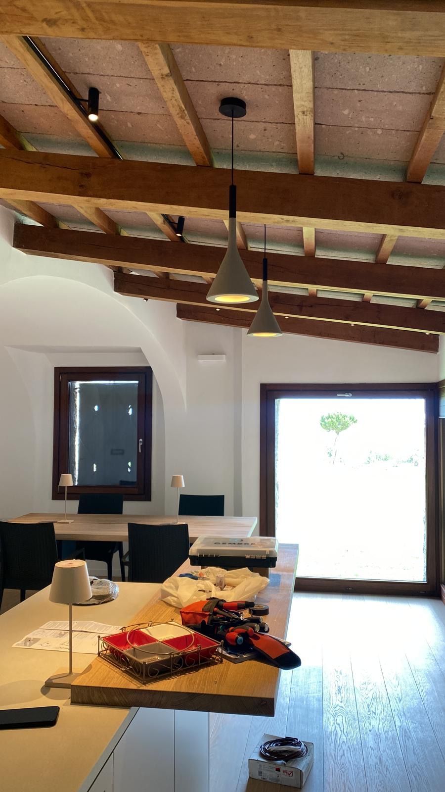 Sala da pranzo rustica con travi in legno, lampade a sospensione, tavolo apparecchiato e un'ampia e luminosa porta d'ingresso.