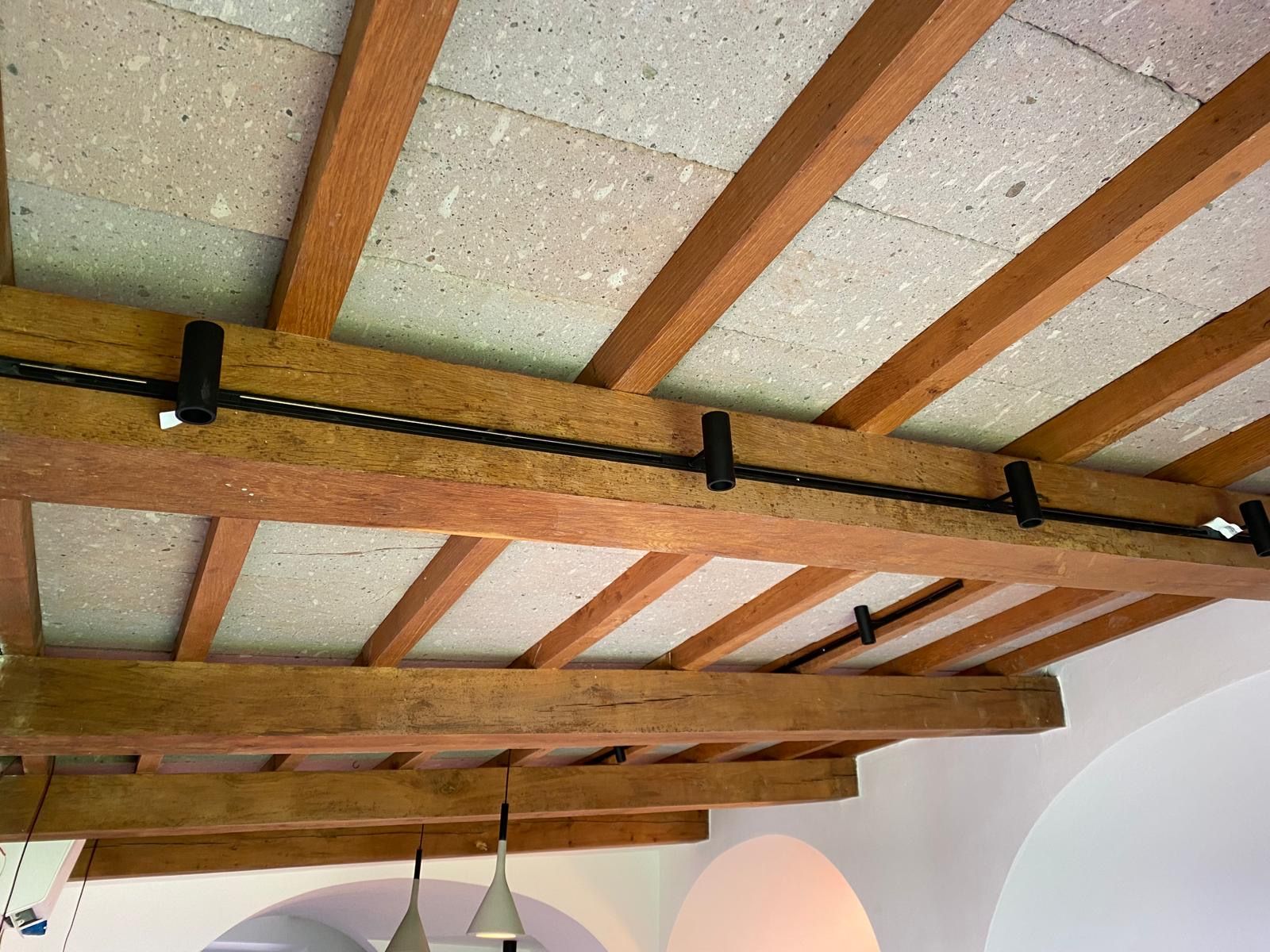Travi in legno a soffitto con un cavo nero che attraversa un angolo del soffitto bianco