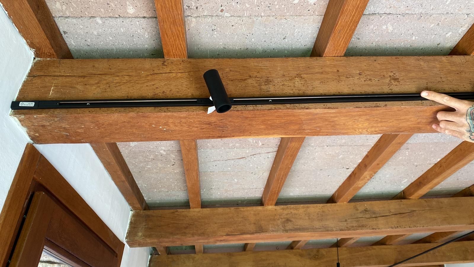 Una mano impugna una lunga asta nera contro una trave di legno del soffitto all'interno di una stanza.