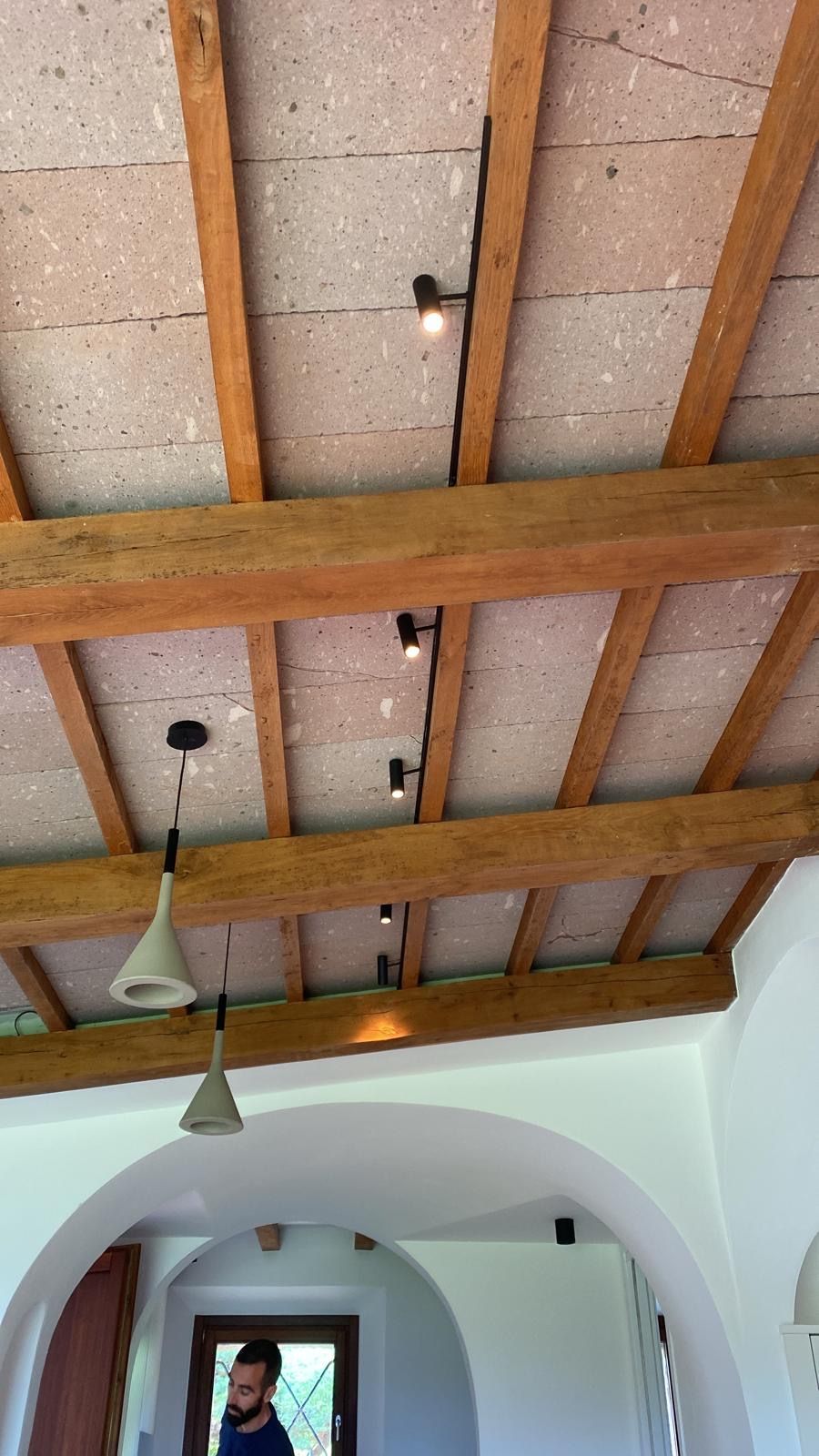 Soffitto con travi in legno a vista, pannelli isolanti rosa e lampade a sospensione sopra un interno ad arco.