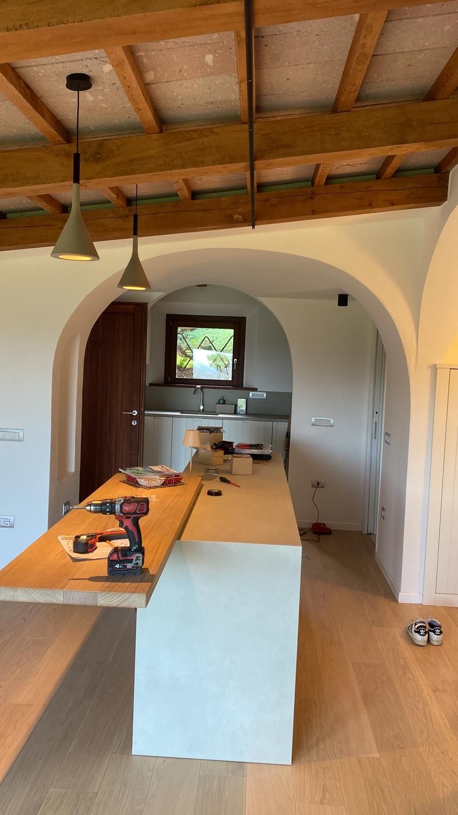 Cucina moderna con lunga isola centrale, lampade a sospensione, soffitto in legno e porta ad arco.