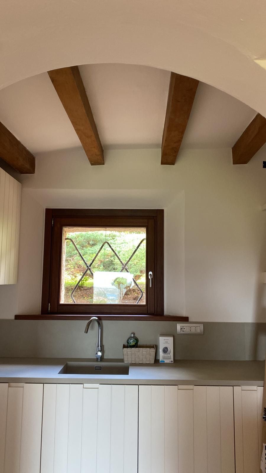 Cucina compatta con travi a vista sul soffitto, piccola finestra, lavello e mobili bianchi.
