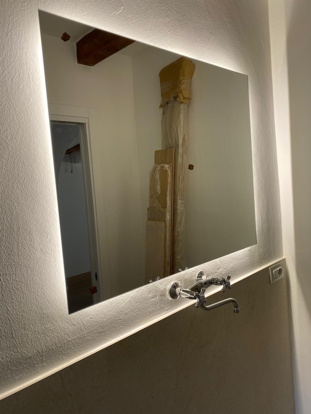 Specchio da bagno con lavabo e rubinetto a parete che riflette una porta e una parete non rifinita.